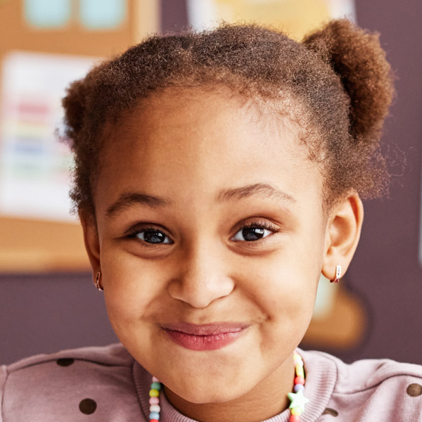 A girl with curly hair and playful earrings smiles warmly, radiating happiness.