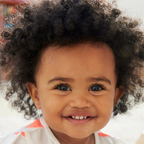 A cheerful child with curly hair beams with a wide smile, radiating happiness.