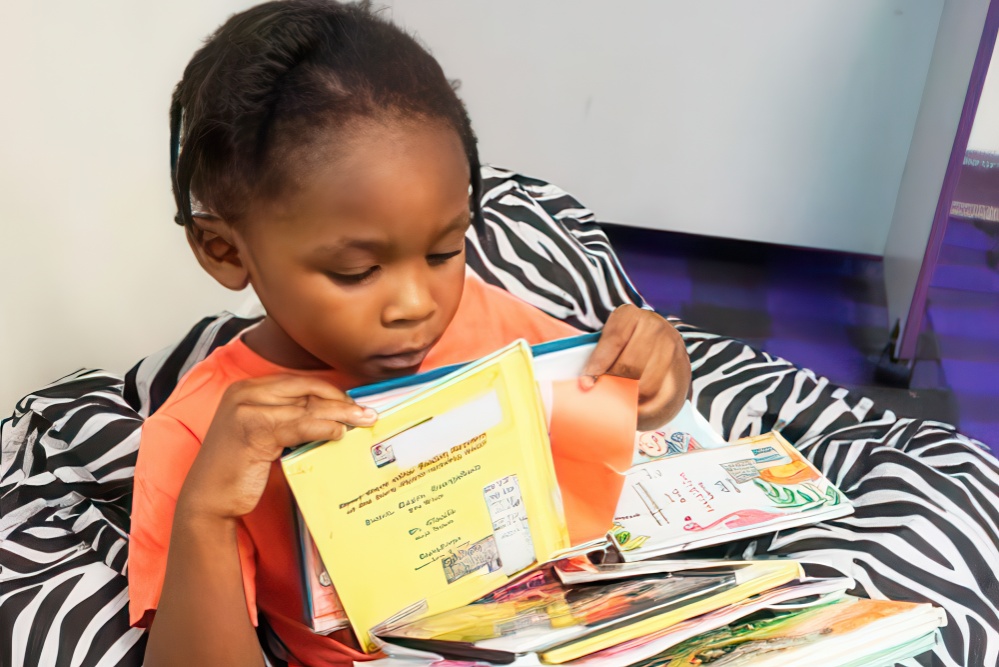 Young child exploring colorful books with curiosity while sitting on a comfy chair.