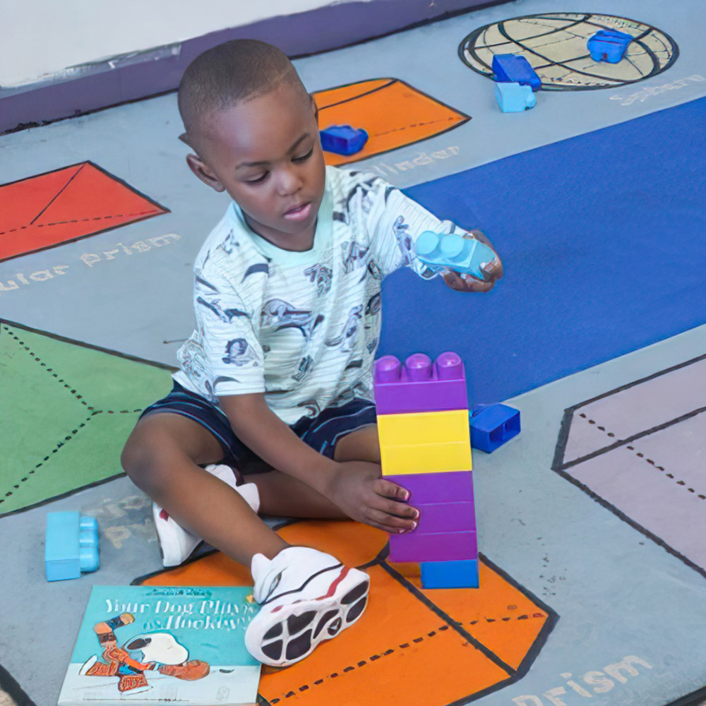 A boy concentrates on building a tower with colorful blocks, focused on his construction.