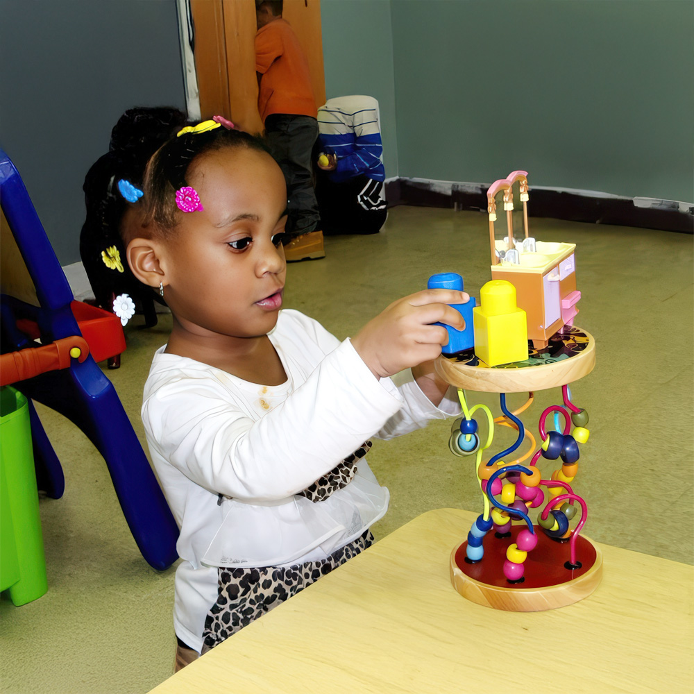 A young girl carefully stacks colorful blocks, focused on her play at a table.