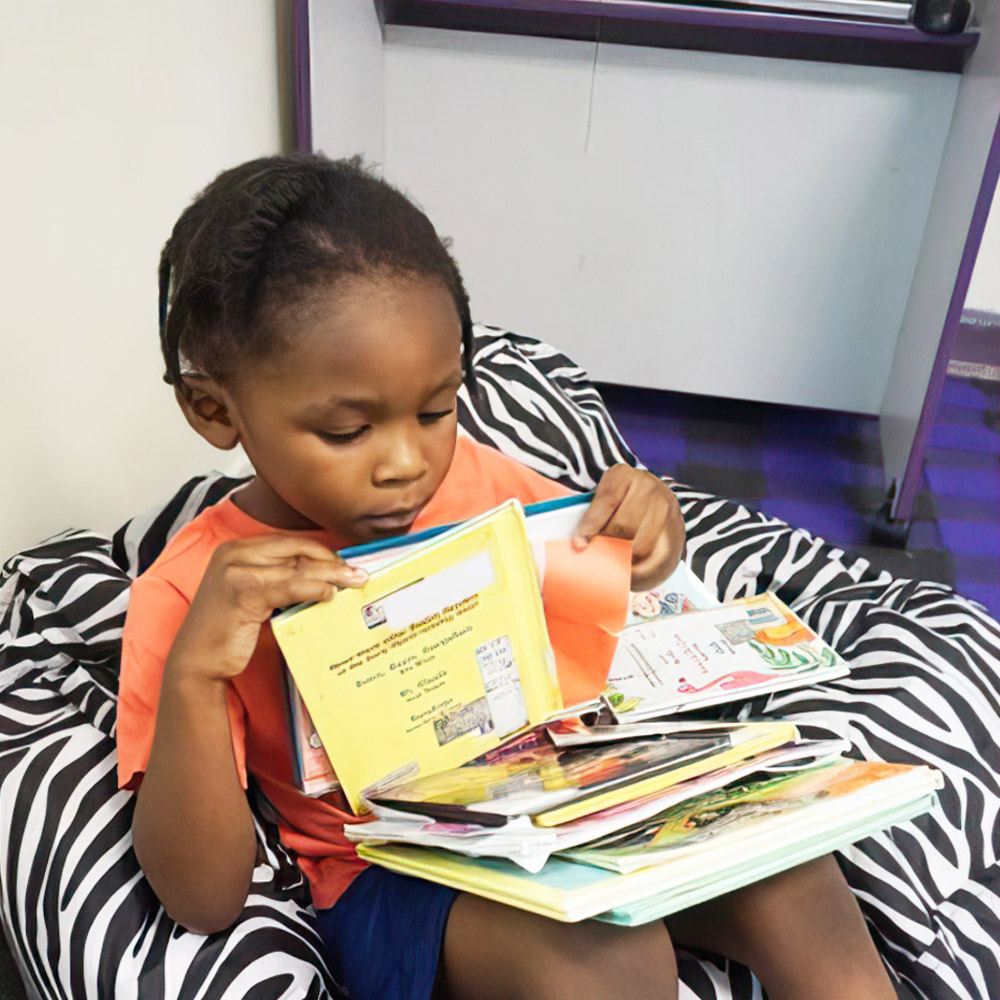 A child sits with a stack of colorful books, intently looking through them.