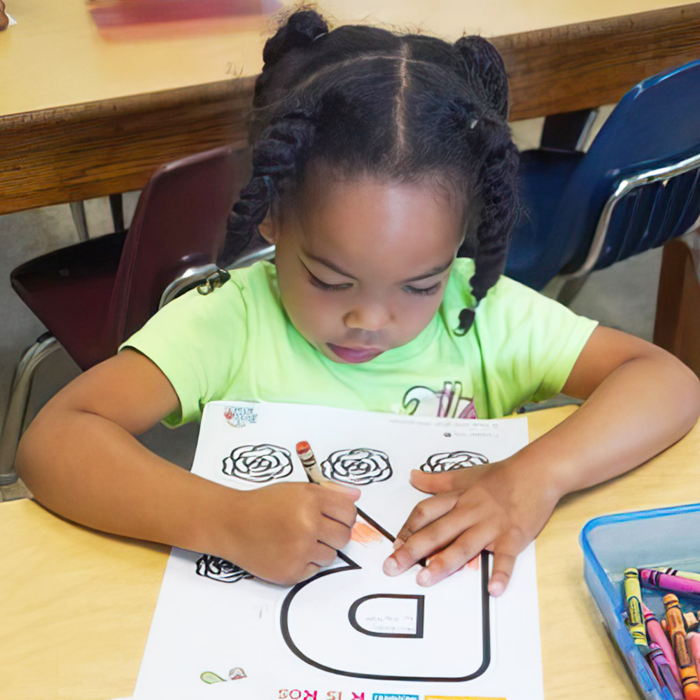 A young girl is focused on coloring a sheet, carefully using a crayon with concentration.