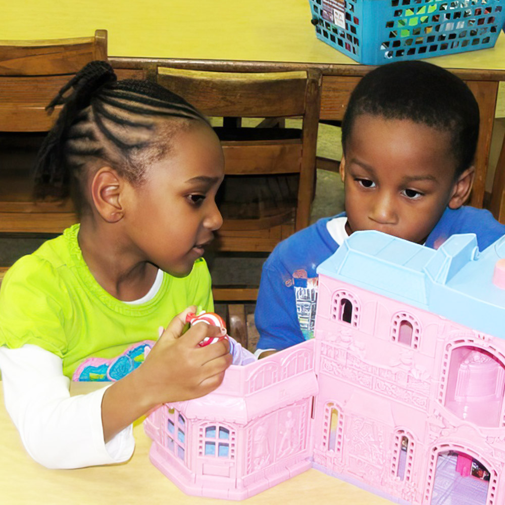 A girl and boy play with a dollhouse, deeply engaged in their imaginative play.