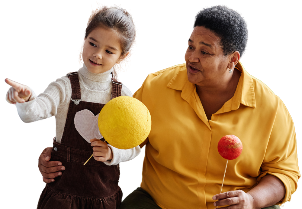 A girl excitedly points while an older teacher smiles, both holding colorful crafts against a soft background.